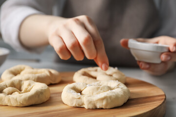 Woman adding sea salt onto uncooked pretzels at table indoors, closeup