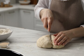 Making pretzels. Woman cutting dough at table in kitchen, closeup