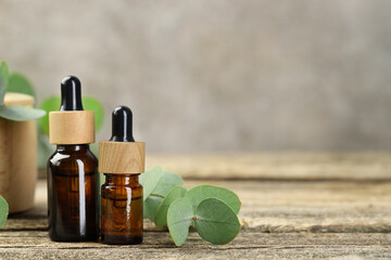 Bottles of essential oil and eucalyptus leaves on wooden table, closeup. Space for text