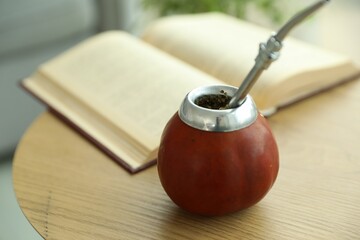 Traditional yerba mate tea and book on wooden table indoors, closeup