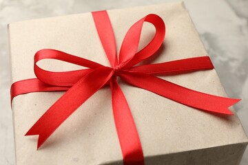 Gift wrapped in kraft paper with bow on grey textured background, closeup
