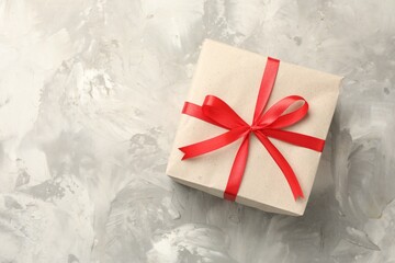 Gift wrapped in kraft paper with bow on grey textured background, top view. Space for text