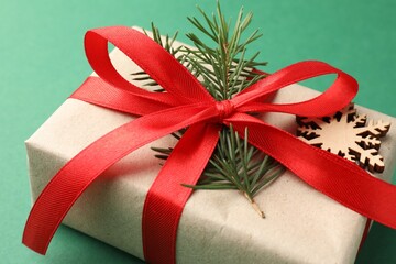 Gift wrapped in kraft paper with bow, ornament and fir tree branch on green background, closeup
