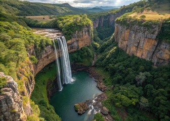 Lush greenery frames a panoramic aerial of a majestic waterfall plunging into a tranquil pool, amidst rugged cliffs.