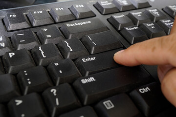 Close-up of a hand pressing the Enter key on a computer keyboard, showcasing the textured black...