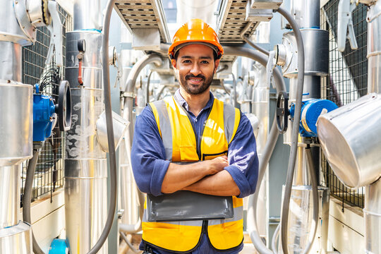 Male technical foreman in safety uniform inspection maintenance holding a laptop while look at camera and smile on the roof of a building, Industrial background, Stand confidently and cross your arms