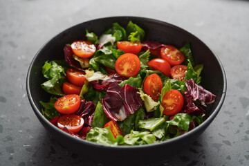 Salad with green and purple leaves and cherry tomatoes in black bowl