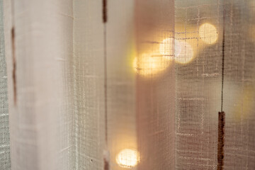 Close-up of soft sheer curtain with warm bokeh lights in the background. Cozy home atmosphere, elegant texture, soft focus concept for interior design and minimalist lifestyle inspiration.