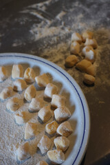 Handmade italian traditional potato Gnocchi ready for cooking on a plate on wooden table