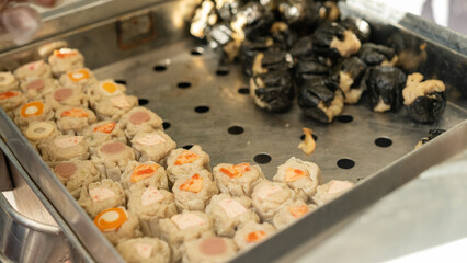Close up of uncooked dim sum arranged in a metal tray, fresh handmade street food with various fillings, soft texture and savory appearance, Asian culinary preparation at local food market.