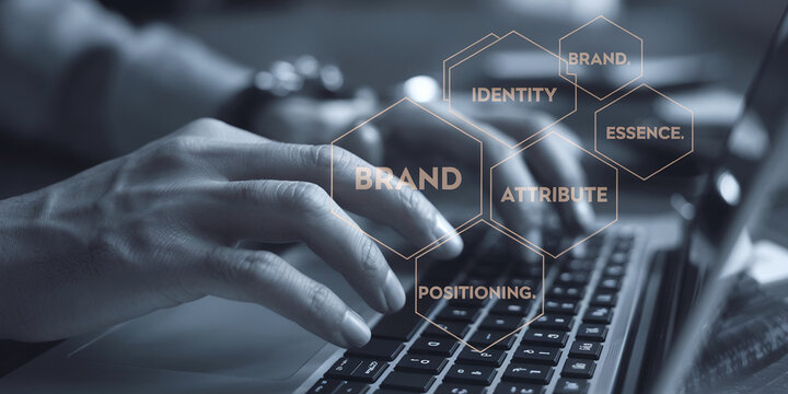 Close-up of hands typing on a laptop keyboard, overlaid with brand identity hexagons highlighting concepts like brand, attribute, essence, positioning, and identity, symbolizing digital marketing and 