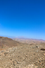 Desert mountain peak rising over barren plain under blue sky