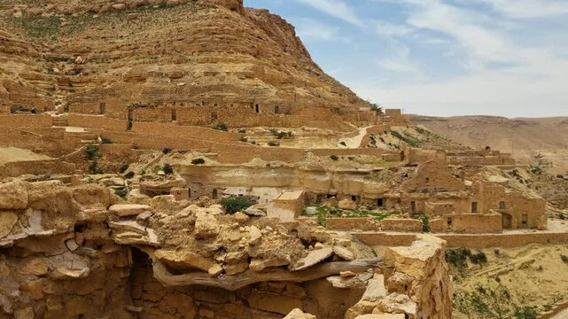 View over the rugged, sun-scorched slopes of the Saharan Atlas Mountains, with the historic Berber village of Chenini nestled among the rocks, a timeless desert settlement in Tunisia