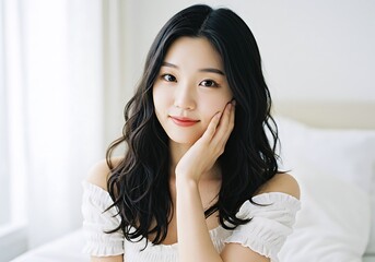 A young Asian woman poses in a bright room filled with natural light. Her long wavy hair complements her soft features as she lightly rests her hand on her face, conveying a calm and serene mood