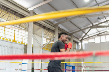 Boxer training on boxing ring, wearing red boxing gloves, smiling and practicing punches