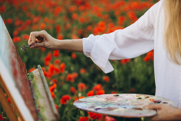 Woman artist painting in poppy field using palette knife