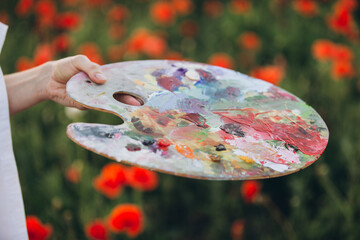 Painter holding palette with colorful oil paint in poppy field