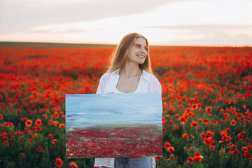Young artist holding painting in poppy field at sunset