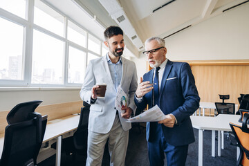 Senior and junior businessmen discussing financial reports in modern office