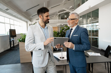 Smiling businessmen using tablet and discussing project in modern office