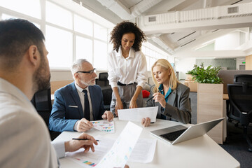Smiling, happy businesspeople working together analyzing financial charts and documents in office