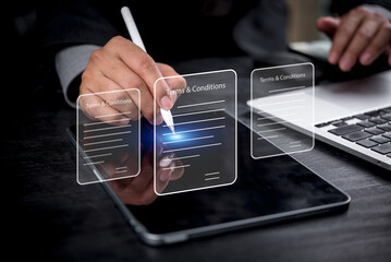 Businessman digitally signing terms and conditions on a tablet, with holographic icons representing...