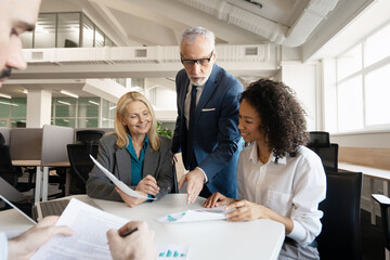 Smiling, confident group of multinational team analyzing financial reports in modern office