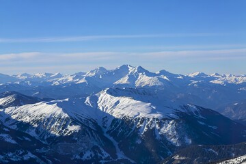 A panoramic photograph of snow-covered mountain ranges under a clear blue sky.