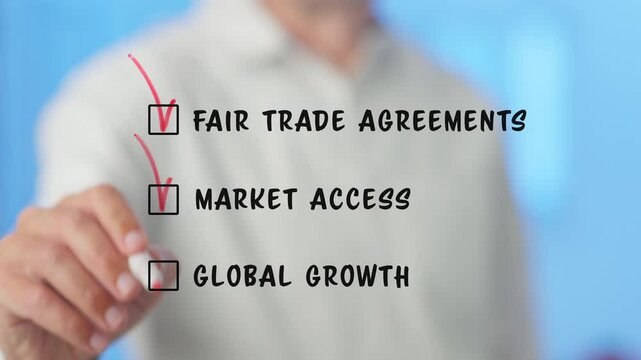Businessman marking checkboxes for fair trade agreements, market access, and global growth, presented on a transparent screen against a blurred blue background