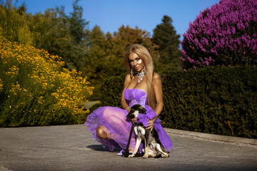 Beautiful, shapely woman in elegant luxury dress sensually walks with her dog in the city on a...