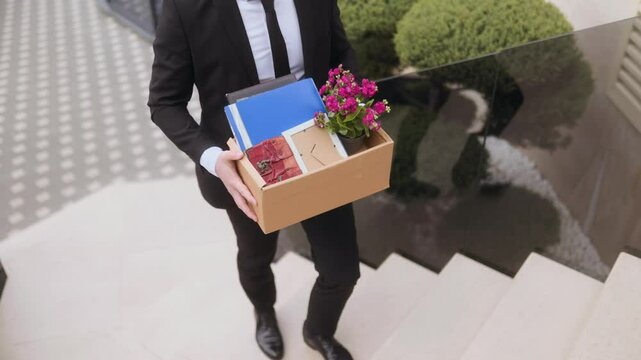 Businessman carrying box of personal items and flowers down stairs