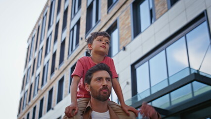 Joyful dad piggyback kid in urban district closeup. Man hold smiling child boy