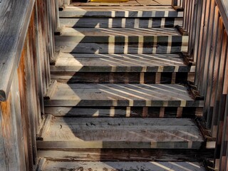 sturdy wooden stairs ascend beside tranquil lake, adorned with intricate shadows cast by the...