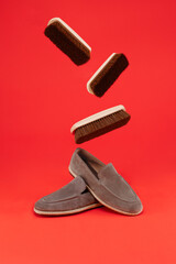New of suede loafers pair of boots with flying shoe brushes on a orange background.