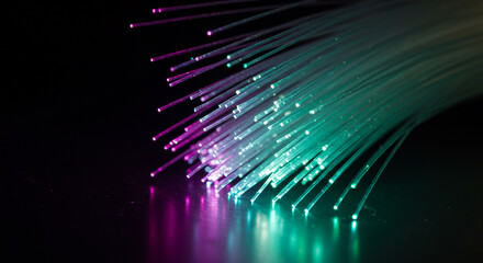 Close up of fiber optic cables with green and purple light against a black background reflecting light