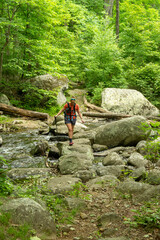Fototapeta premium Woman Steps Over Large Boulders to Cross Creek in Shenandoah