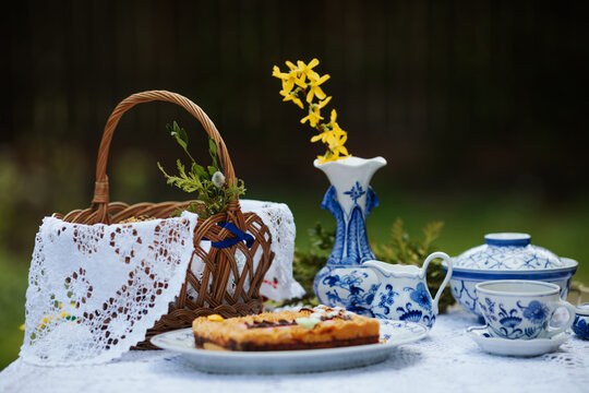 Easter still life with flowers, cake, wicker basket and porcelain on the table 