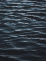 A dark, textured image of undulating water, evoking a sense of calmness and depth. The rippling surface of the water reflects the light, creating a mesmerizing pattern