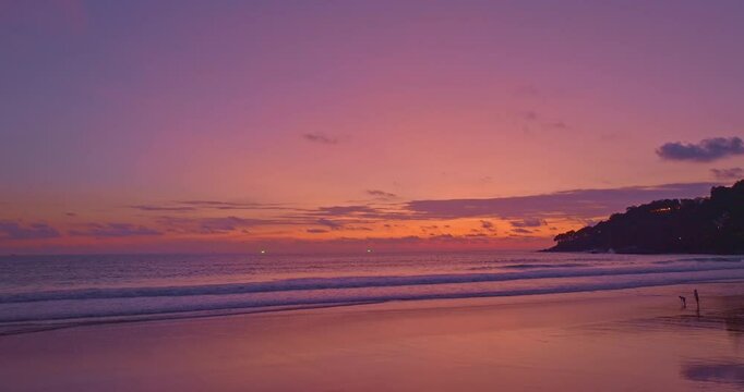 A breathtaking sunset over a tropical beach, casting golden hues across the sky and reflecting on the calm ocean waters. Silhouettes of people walking along the shore add a peaceful and serene