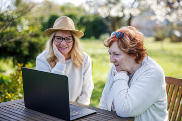 Happy moment of smiling woman with her senior mother while watching laptop screen in garden