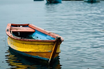 Obraz premium Weathered Wooden Boat Floating On Calm Water With Yellow And Blue Paint