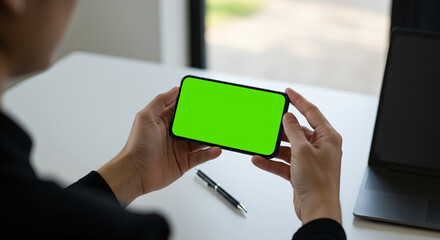 Holding Mobile Phone with Green Screen Over Desk