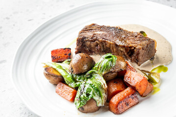 A succulent piece of meat served with a creamy sauce, accompanied by roasted carrots, potatoes, and fresh greens. The elegant plating highlights the gourmet quality of the dish.