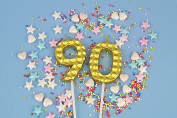 Gold birthday candles and many colorful sprinkles on blue background. Number 90.