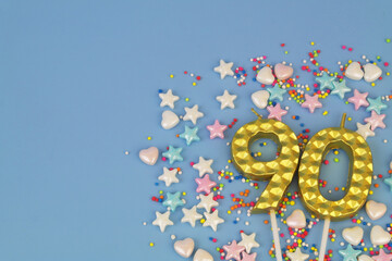 Golden birthday candles and sprinkles on blue background. Number 90. Copy space fo text.