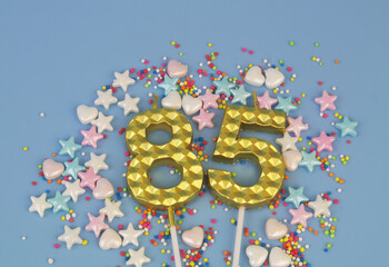 Gold birthday candles and different sugar sprinkles on blue background. Number 85.	