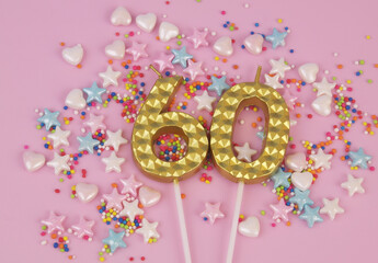 Gold birthday candles and colorful sprinkles on pink background. Number 60.
