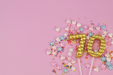Gold birthday candles and many colorful sprinkles on pink background. Number 70.	