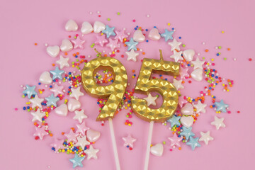 Gold birthday candles and many colorful sprinkles on pink background. Number 95.