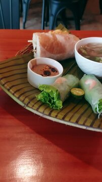Handheld video showing off authentic traditional local Vietnamese dishes pho bo or beef noodle soup, banh mi or baguette sandwich and goi cuo or fresh spring roll